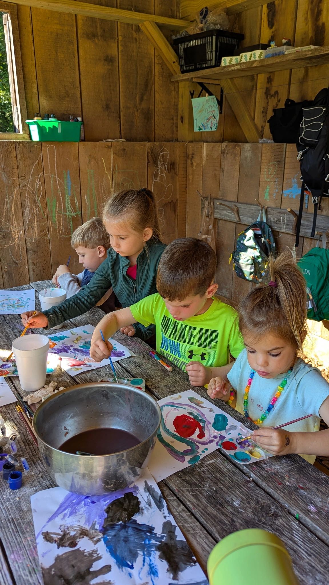 Four children painting enthusiastically at a rustic wooden table in a cozy cabin.