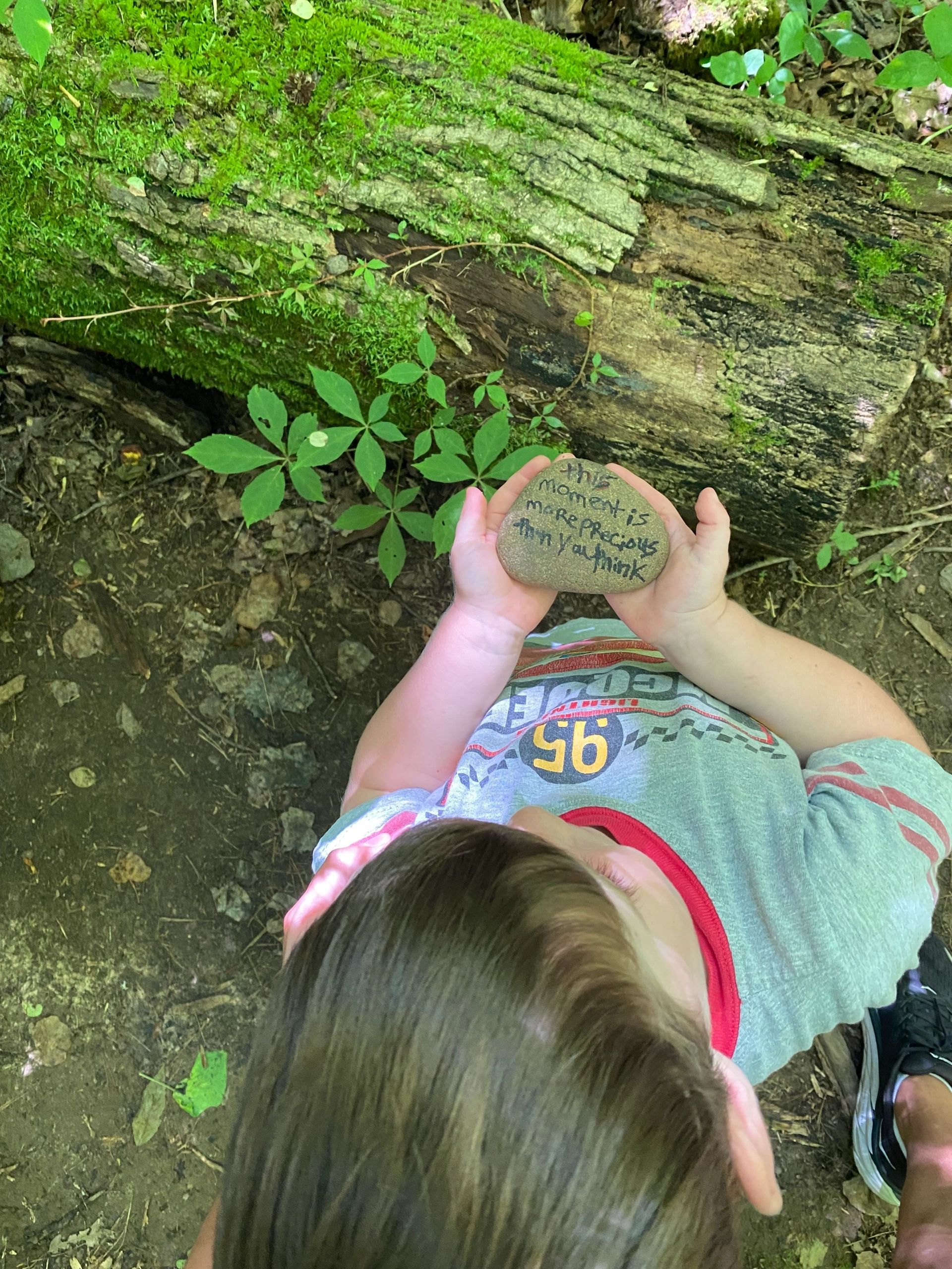 Child holding a rock with a handwritten message in a forest setting.